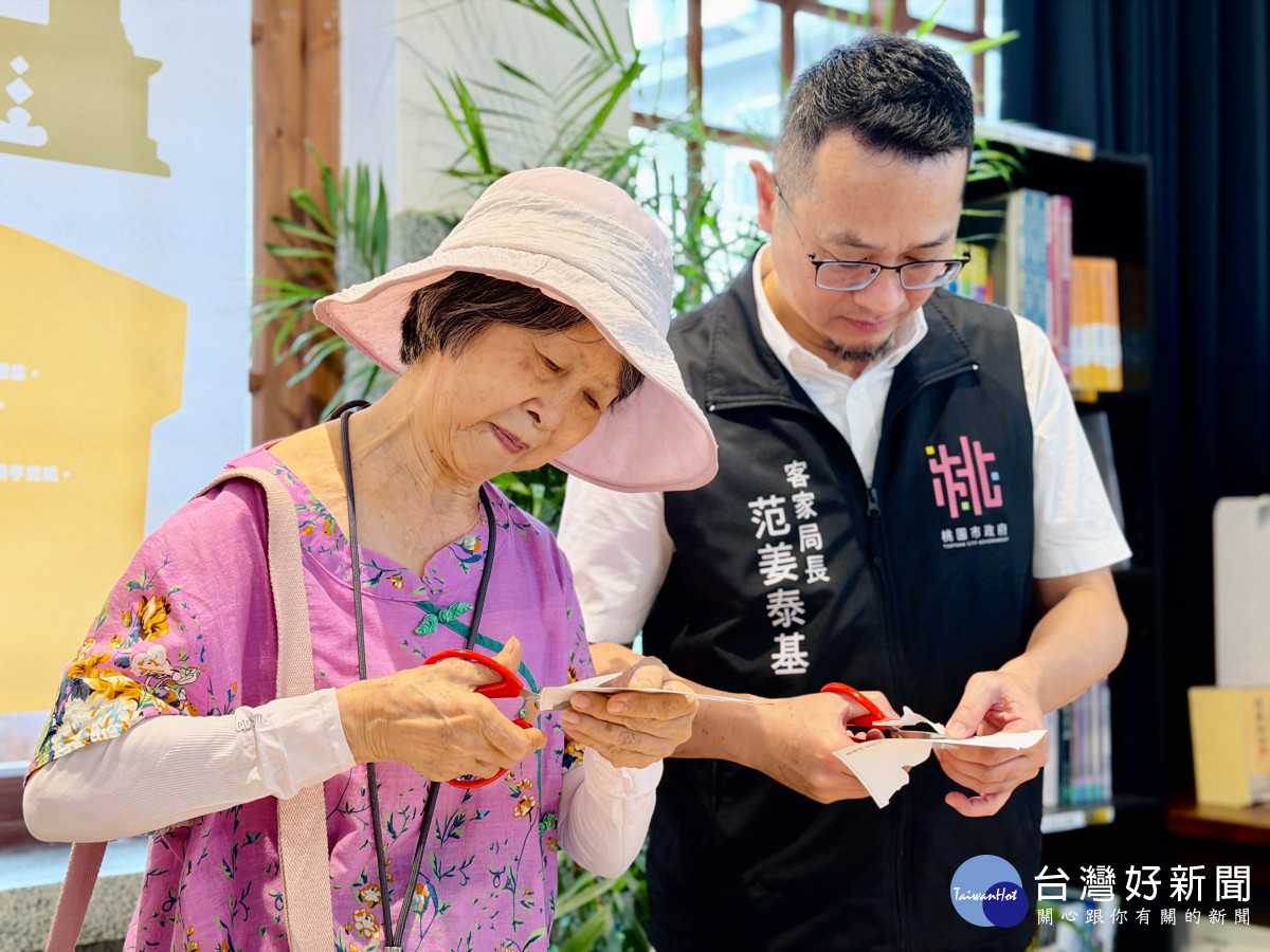 客家局長范姜泰基(右)及李南華女士(左)共同體驗漢聲雜誌曾介紹的剪紙藝術,現場剪出聖蹟亭的剪影。