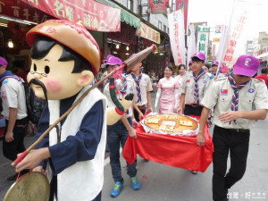 由厚德堂特製的超級大餅「幸福狀元餅」，在報馬仔公仔引領下於朝聖大道商圈繞了一圈，吸引遊客爭相拍照。（記者蘇榮泉攝）
