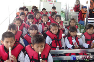 七股龍山國小學童坐船遊潟湖，並用直笛吹奏七股的美龍山之歌歌曲。