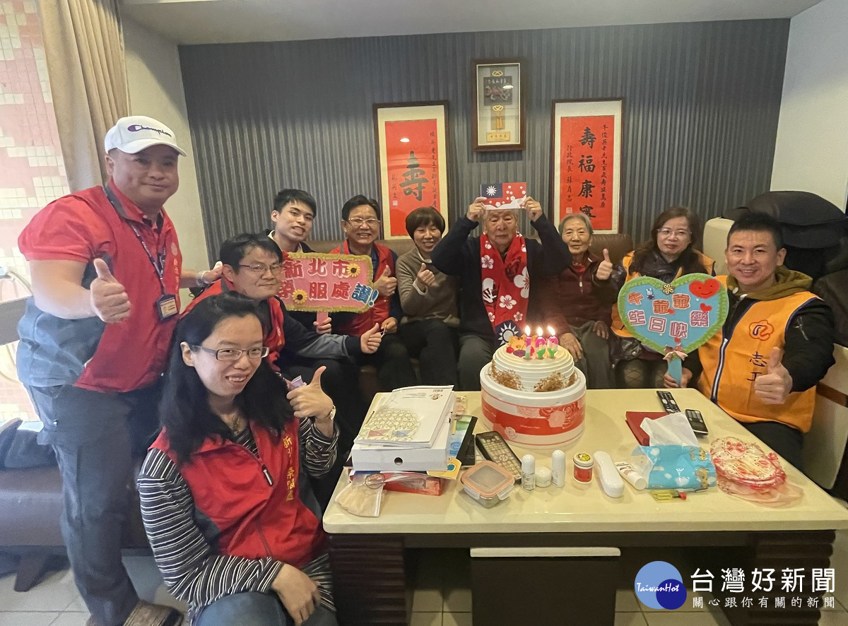 李復鄉總幹事(左5)率同仁及榮欣志工為牛爺爺(中)慶賀百歲壽辰，牛奶奶(中右)及女兒(中左)陪伴在側一同慶生，牛爺爺開心地高舉榮民榮眷基金會國旗口罩合影
