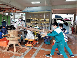 淡水國小學童推動古代農具「土礱」，認識碾米的過程，體驗古早爆米香的傳統技藝，同時一邊學臺語
