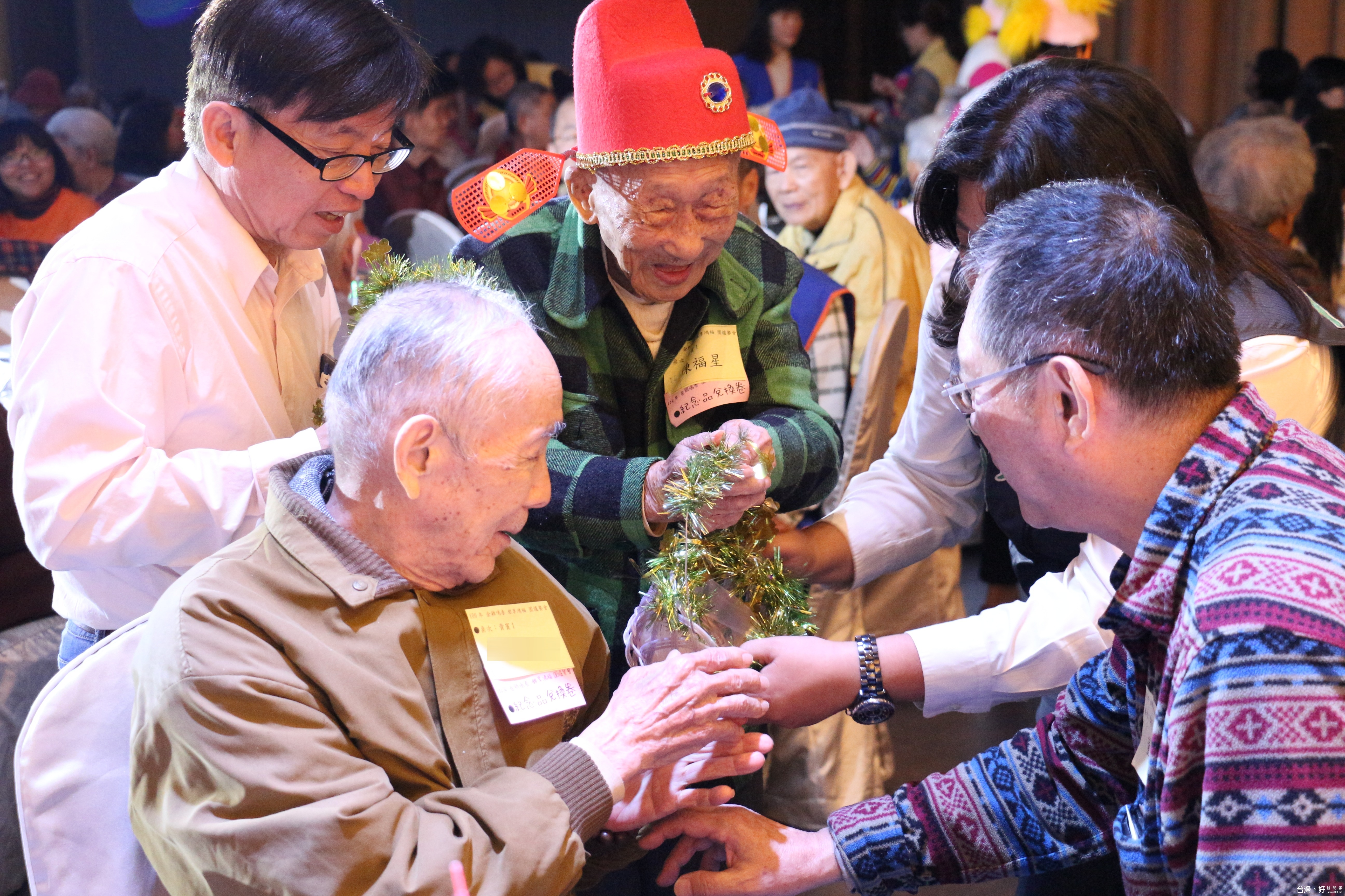 百歲人瑞福星阿公(戴紅色福星帽者)和其餘幾位長輩在餐會中發送代表福氣的糖果給參與者,希望大家年年都來參加餐會。