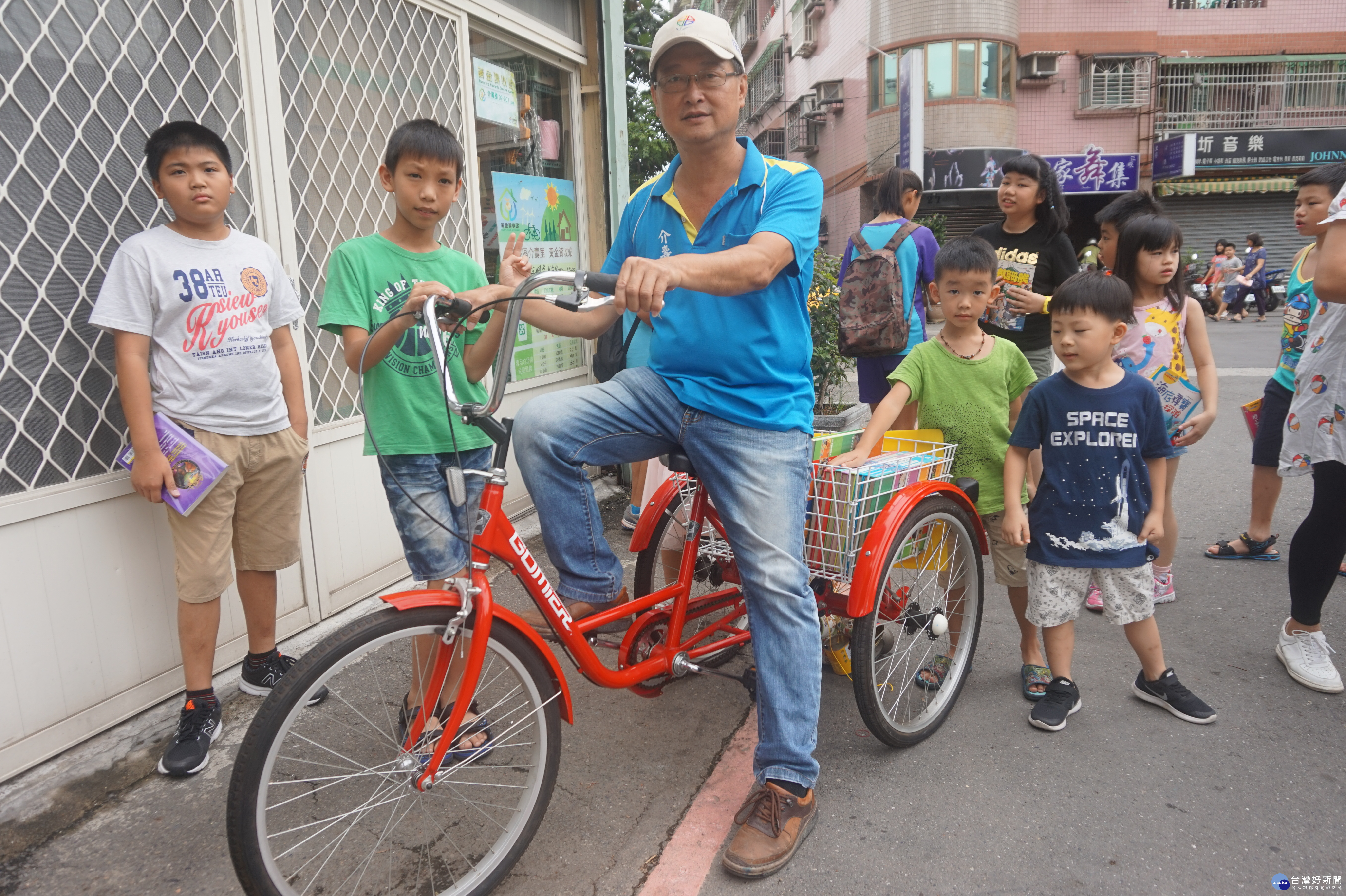 王錫川（戴白帽者）將回收的三輪鐵馬改造為行動漂書車，架上放滿舊書籍沿路漂書。路上小朋友看到顏色繽紛的各類書籍，總是揮手要里長伯停車，挑到喜歡的還可以免費帶回家。各