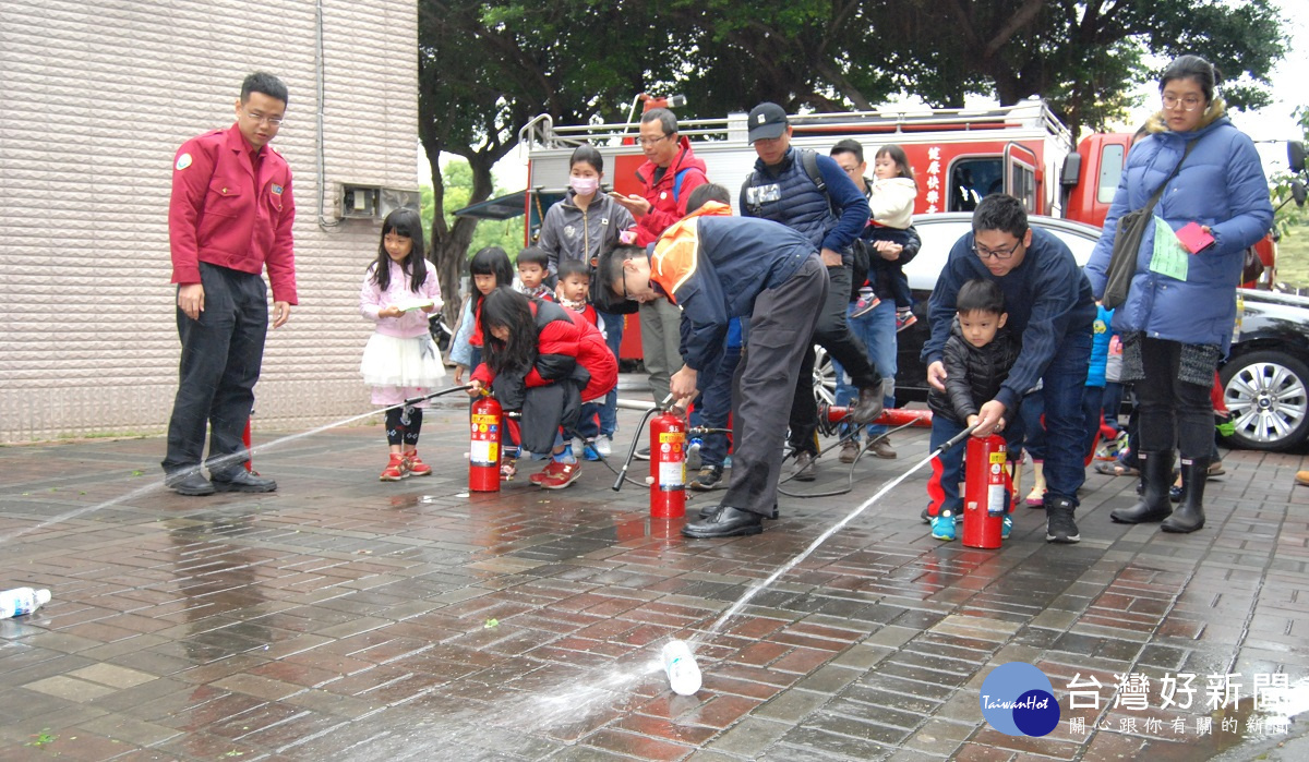 在消防人員協助下家長帶領小朋友學習滅火器操作噴水體驗。