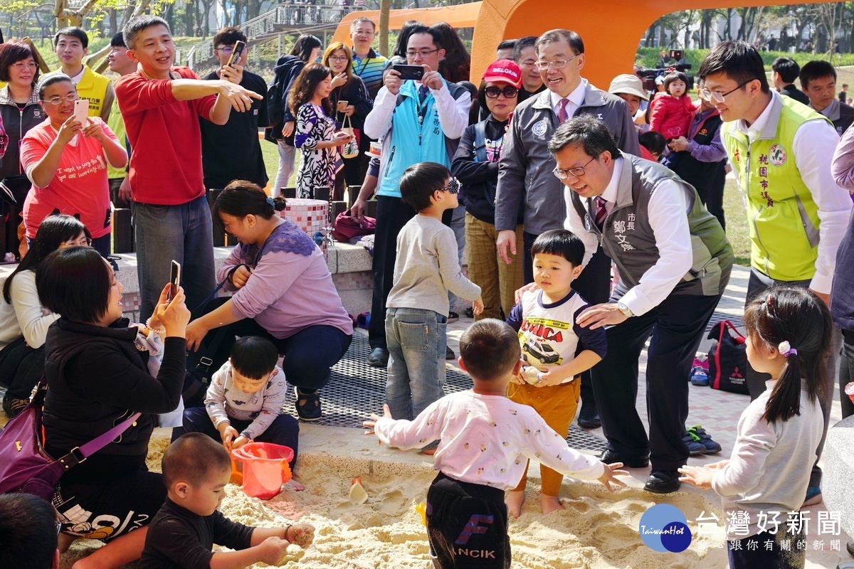 桃園市長鄭文燦在沙池中和嬉戲中的小朋友同樂。