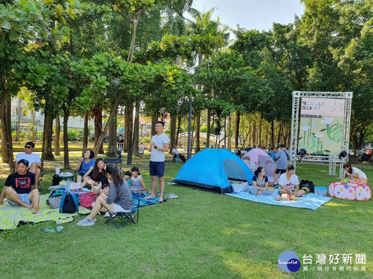 民眾在公園草皮鋪上野餐墊，邊野餐邊看表演，氣氛熱鬧。
