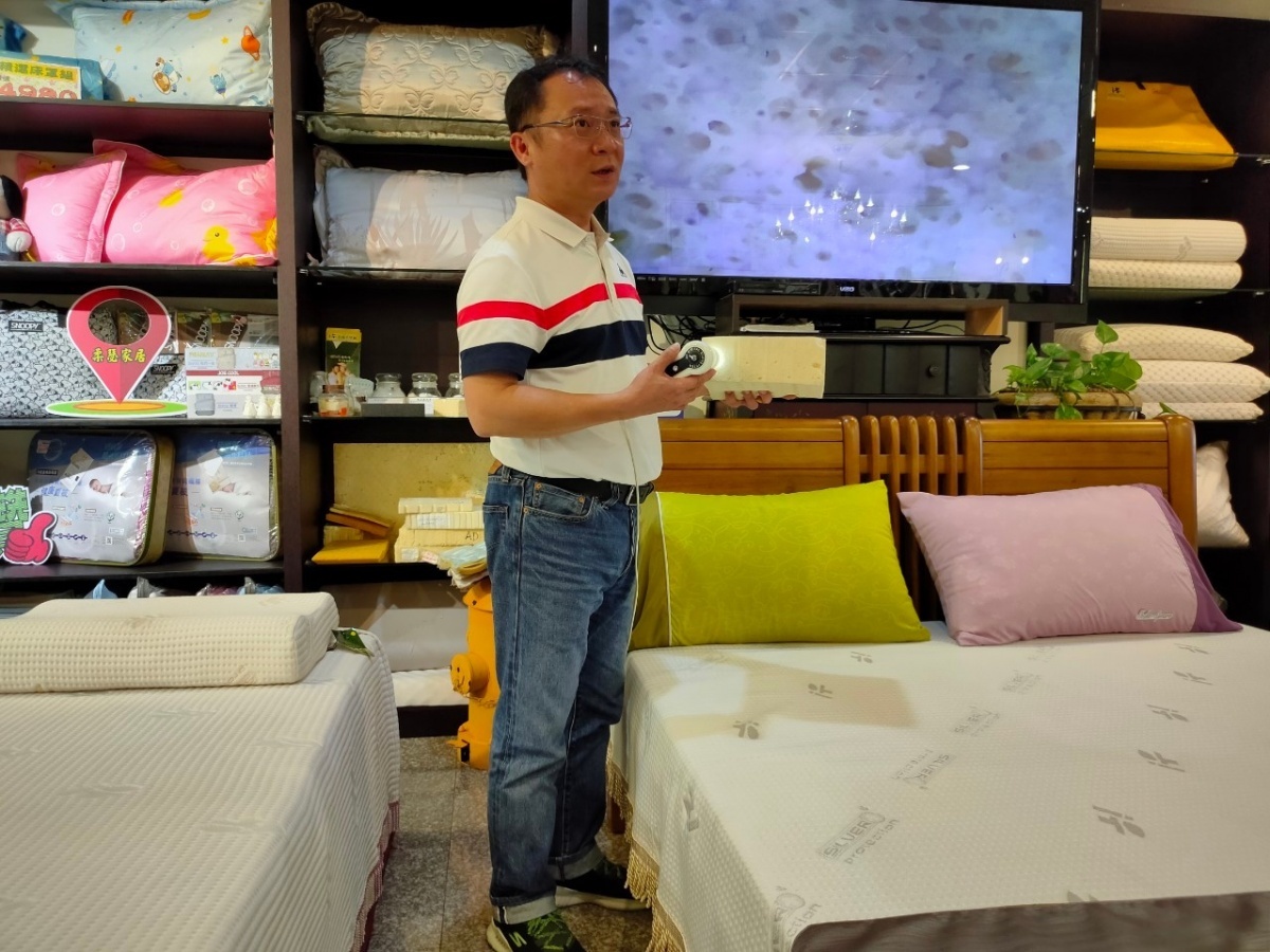 王興鈞用高倍數攝像鏡頭搭配大螢幕,來跟客戶解釋天然乳膠呈現的模樣。(圖/陳宏林攝)